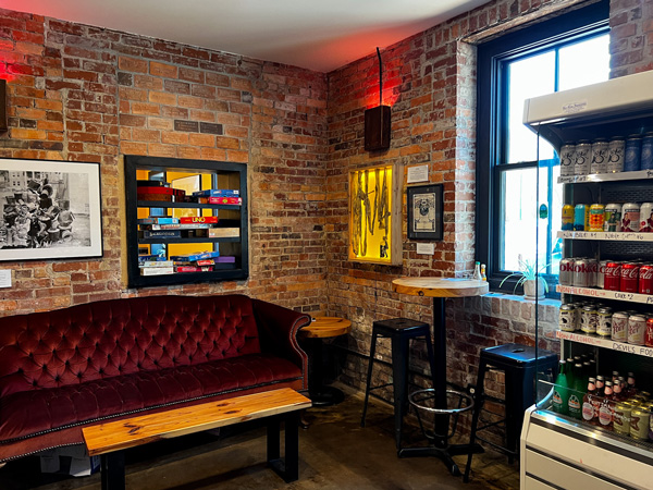 Zadie's Market in Marshall, NC Bar Area with fridge with beverages, red couch, high top table, and art on the walls