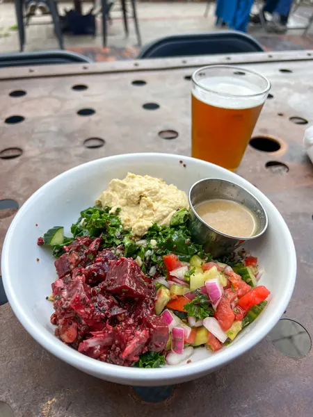 Zadie's Market Restaurant in Marshall, NC Rainbow Bowl with Zadies Market Restaurant Marshall NC Rainbow Bowl with faro, quinoa, tomato, cucumber, hummus, and beets over kale in white bowl next to an amber beer on table
