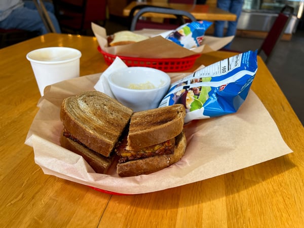 Zuma Coffee in Marshall NC Vegan Sandwich with tempeh, side of sauerkraut, bag of chips, and latte in paper cup in red basket with paper