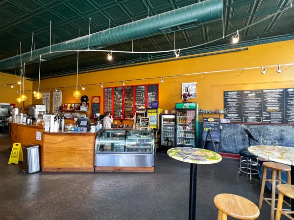Zuma Coffee Restaurant in Marshall North Carolina with gray brown floor, counter with register, baked goods, and coffee and smoothie menu behind it