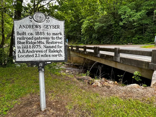 Andrews Geyser in Old Fort NC Road Sign with information about the fountain in front of stream with bridge and road