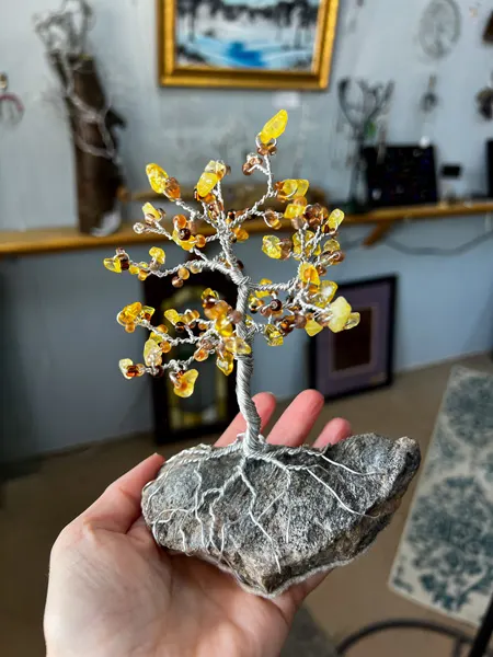 Arrowhead Gallery & Studios in Downtown Old Fort NC with white hand holding up a sculpture of a tree with a rock base, orange gemstones, and twisted wire for branches