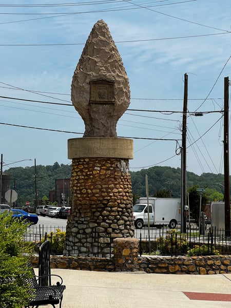 Arrowhead Monument in Downtown Old Fort, NC with stone and concrete statue in shape of arrowhead with electrical lines, street traffic, and blue sky