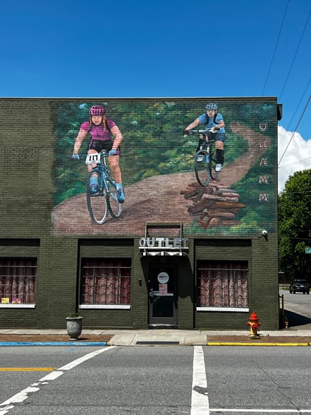Downtown Old Fort Biking Mural on top of building with two bikers on dirt pathway