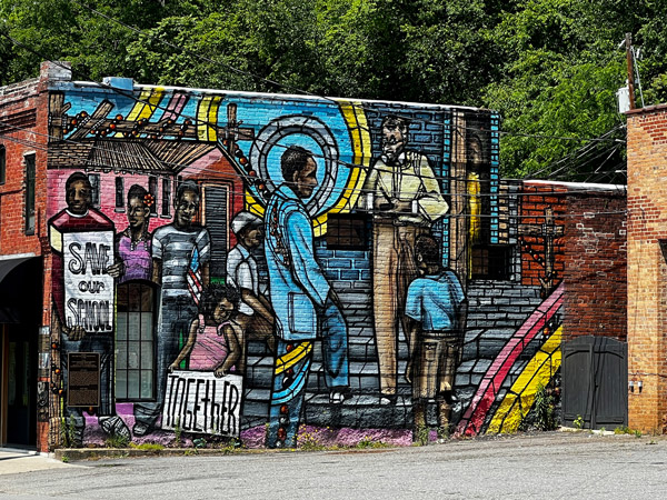 Downtown Old Fort NC Mural with Black children, bright color homes and sky, and signs that say save our school together