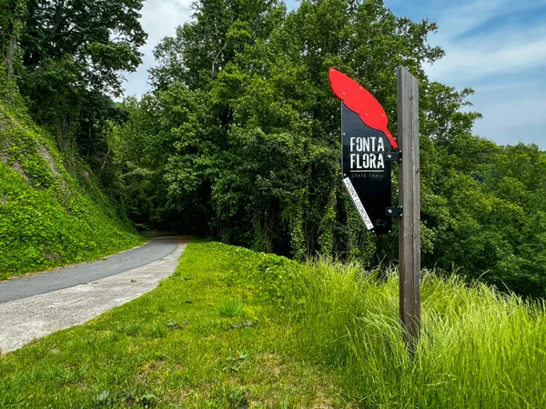 Fonta Flora State Trail Point Lookout Old Fort NC Marker with paved single track pathway surrounded by green grass and trees with large trail sign with red feather