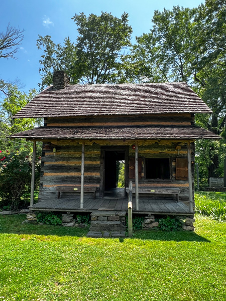 Mountain Gateway Museum historic wooden cabin with roof and porch roof in Old Fort NC with green grass, trees, and blue sky