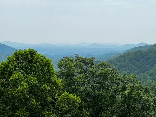 Old Fort NC Point Lookout Trail Overlook with green trees and white, gray, and ombre blue hued mountains in the distance with overcast sky