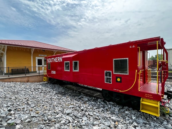 Old Fort North Carolina red Caboose next to former yellow Train Depot with rocks underneath and blue cloudy sky