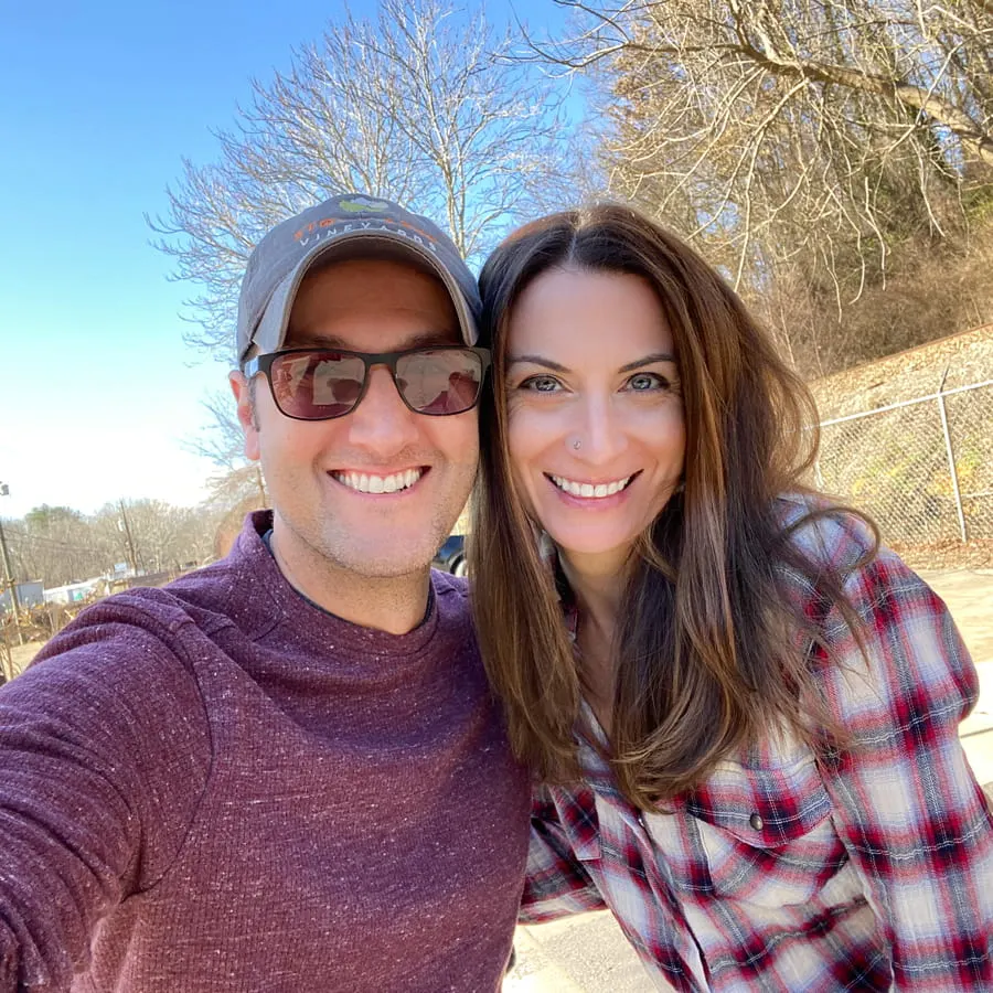 Christine and Tom of Uncorked Asheville with white brunette male in sun glasses, hat, and maroon sweater and white brunette female in red, blue, and white plaid shirt