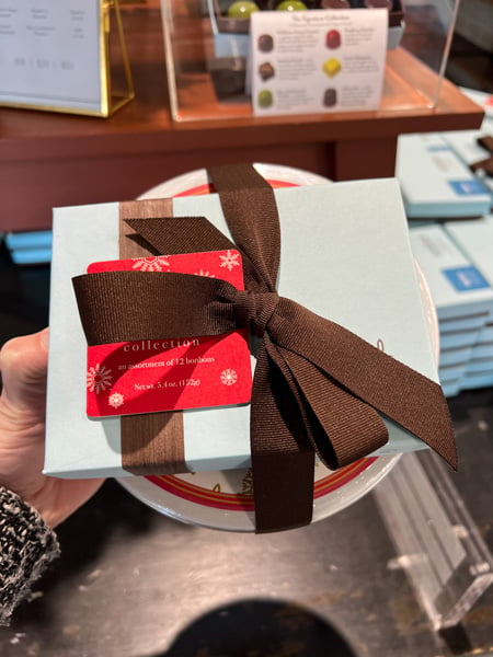 French Broad Chocolate Asheville NC with white hand holding up box of truffles with brown bow and red holiday tag