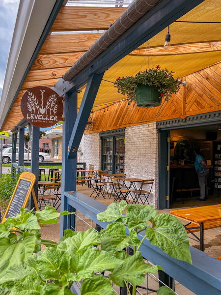 Leveller Brewing Co Weaverville NC Brewery facade with blue railing outdoor covered patio with chairs, tables, and picnic tables along with business sign and green bushes