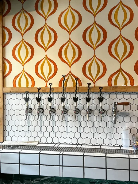Leveller Brewing Co. in Weaverville shovel-themed taps with yellow and orange brown patterned wallpaper in the shape of onions or bulbs