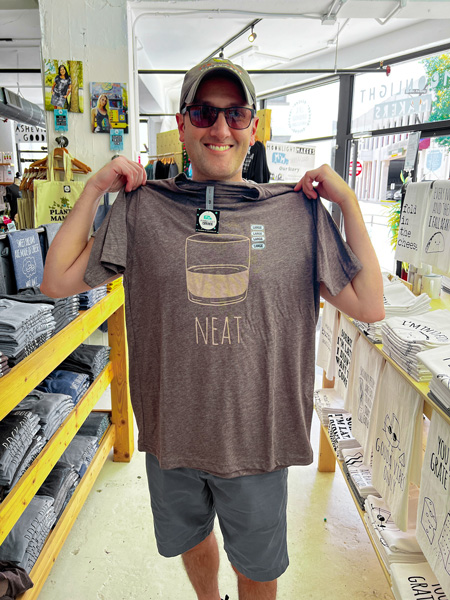 Moonlight Makers Asheville NC white male with hat and sunglasses holding up t-shirt that says neat with image of Old Fashioned cocktail