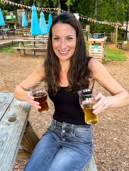 Nest Boutique Asheville NC jeans example with white brunette woman in jeans and black top holding two beers