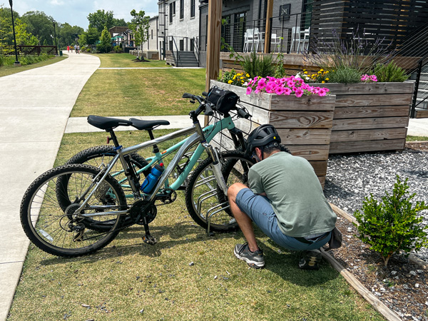 Pangaea Brewing Company Greenville SC Bike Rack along the Swamp Rabbit Trail with male in blue shorts and green t-shirt locking two bikes to rack along the trail