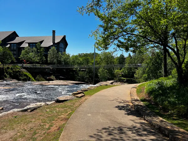 Swamp Rabbit Bike Trail at Falls Park in Greenville SC with paved greenway approaching Liberty Bridge, a suspension bridge of the water