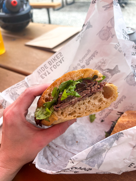 Christine's white hand holding up half of a roast beef sandwich with lettuce, tomato, and mayo at the Swamp Rabbit Cafe and Grocery in Greenville SC (along the Swamp Rabbit Trail)