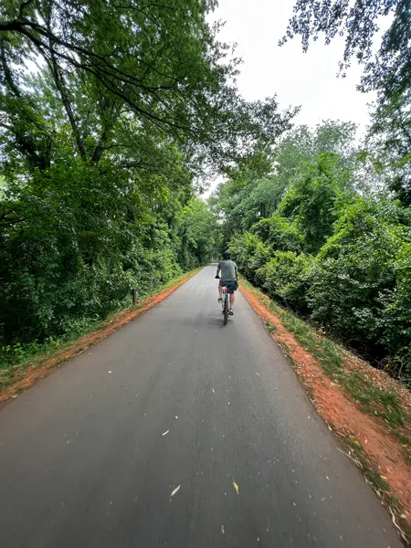 Swamp Rabbit Trail greenway with person Mountain biking down paved asphalt path surrounded by trees