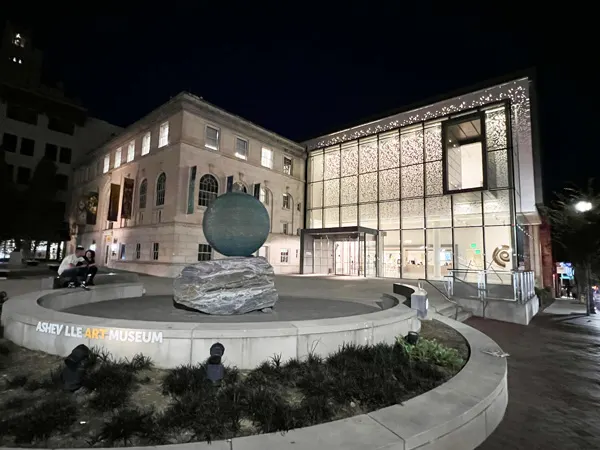 Asheville Art Museum at Nighttime which is a large building full of floor to ceiling windows with blue glass sculpture out front
