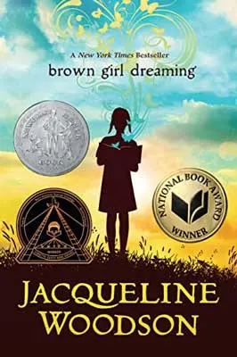 Brown Girl Dreaming by Jacqueline Woodson book cover with shadowed image of person on grass standing and reading a book with blue and yellow sky