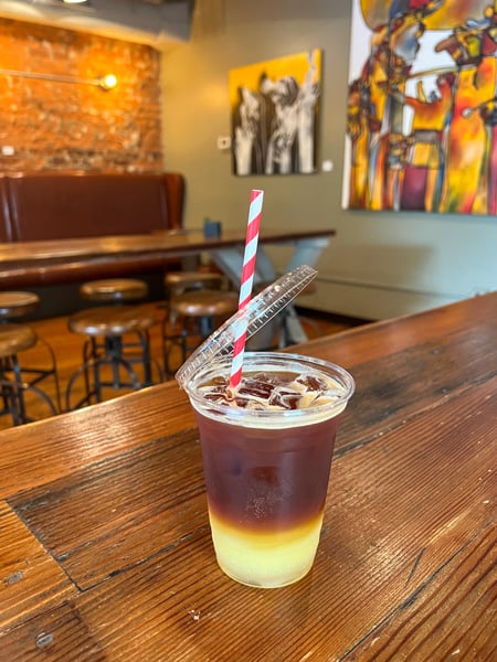 The Rhu Coffee Downtown Asheville NC Restaurant with iced coffee with vegan milk on table with red and white paper straw and wall paintings in background