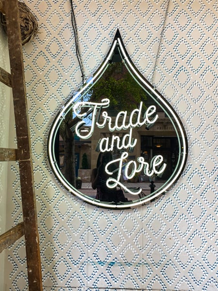 Trade and Lore Coffee Shop Downtown Asheville sign with name in tear drop like icon next to brown ladder on white wall