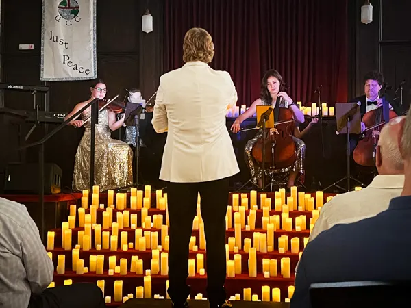 Vienna Candlelight Orchestra in Asheville NC with conductor in white jacket and black slacks in front of faux lit candles and orchestra playing string instruments