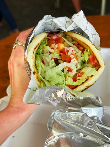 Asheville Greek Festival Gyro in wrapper with falafel, lettuce, and tomato held up by white hand