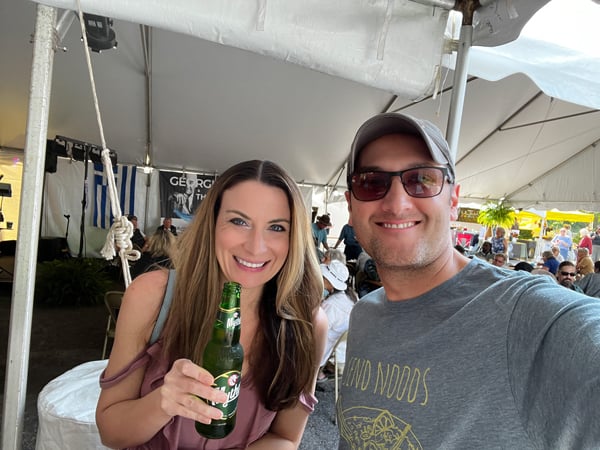 Asheville Greek Festival Music and Dancing Tent with white brunette male and female taking a selfie and female is holding a bottle of Greek beer