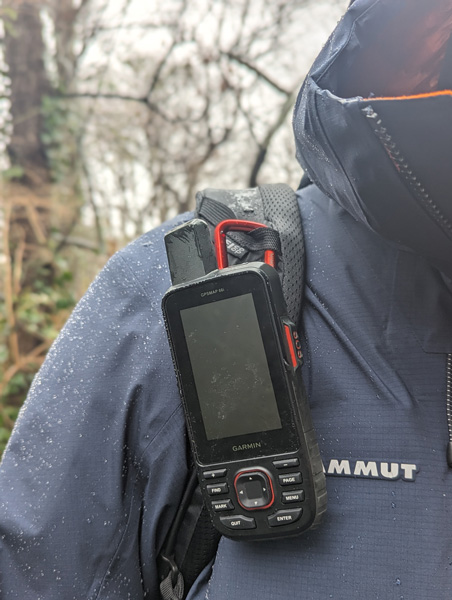 Black Garmin on backpack strap of person hiking in blue jacket