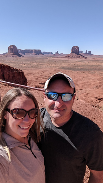 White male and female (Tori) in sunglasses and hiking tops with mountains and dirt landscape in the background