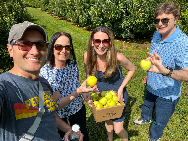 Stepps Hillcrest Orchard in Hendersonville Apple Picking with two white brunette women and two white brunette men in orchard and holding picked apples with box full of apples too