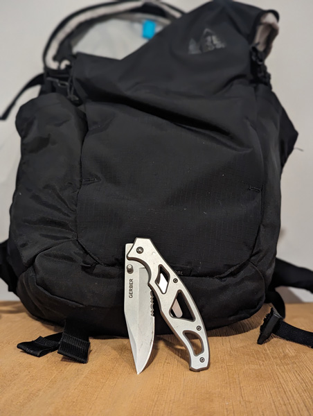 Silver Gerber Pocket Knife in front of black backpack on table