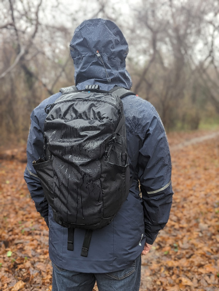 Black Hiking Backpack on person wearing blue rain jacket outside in the rain