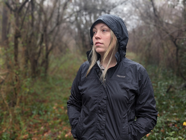 White, blonde woman in black Marmot Rain Jacket in the woods