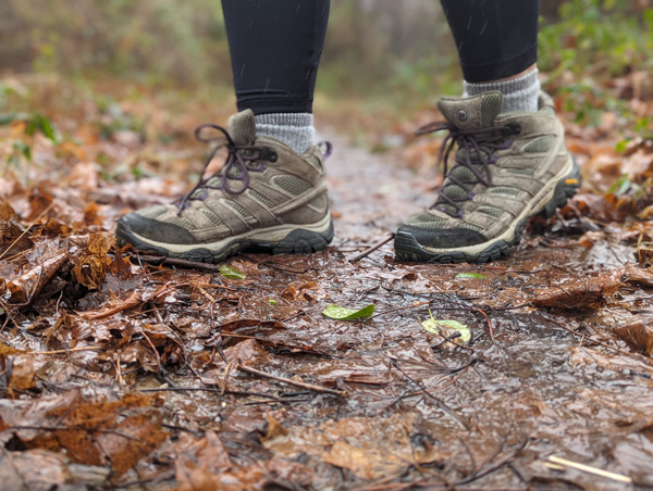 brown Merrell Hiking Boots with purple laces outside on muddy dirt hiking trail