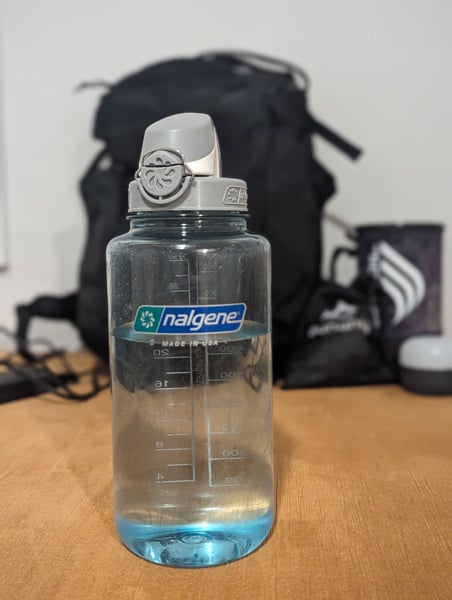 Nalgene Water Bottle on table with black backpack in background