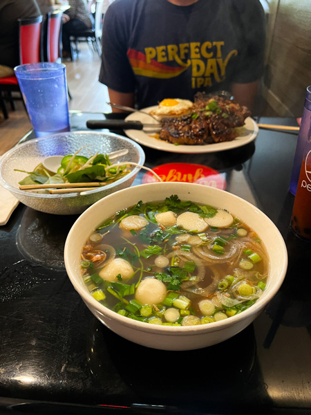 White bowl of pho soup with light brown broth, onions, basil, noodles, and meatballs on table at Wild Ginger Noodle Bar in Asheville, NC